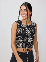 Top corto negro con estampado de flores y figuras geométricas en color crema, con breteles anchos y lazo ajustable en la cintura.