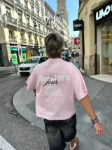 Remera rosa de corte recto con estampado en la espalda que incluye el texto "Itta Tours", "Tour", y nombres de ciudades como Ibiza, Madrid, Andorra, Barcelona y Formentera.
