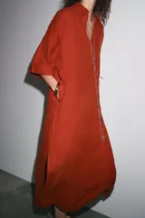 Vestido tipo túnica color ladrillo confeccionado en lino 100%. Tiene cuello solapa, escote pico, manga corta, bolsillos laterales ocultos y bolsillo de parche en el pecho. El bajo tiene aberturas laterales.