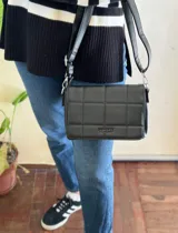 Cartera bandolera de diseño capitoneado, en color negro con correa ajustable.