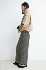 Pantalón de tiro alto con elástico en la parte posterior de la cintura y cierre oculto lateral. Presenta bolsillos discretos en las costuras laterales y piernas anchas con pliegues adelante y atrás. Diseño estampado con motivos geométricos en blanco y negro.