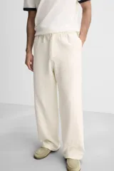 Pantalón color crema de corte amplio, con cintura elástica ajustable con cordón, bolsillos laterales y trasero, cierre frontal con cremallera y botón.