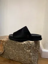 Sandalias bajas de cuero color negro, con suela plana de caucho y logo bordado en el lateral.