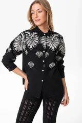 Camisa negra de lino con bordados florales blancos, de corte clásico, cuello camisero y mangas largas con puños abotonados.