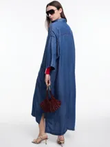 Vestido camisero largo de denim liviano de lyocell azul, de silueta relajada, mangas 3/4 amplias y hombro caído. Cuenta con bolsillos grandes aplicados en el frente, tajos laterales y botones a contratono.