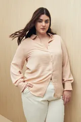 Camisa blanca de manga larga con textura sutil y caída fluida. Presenta cuello clásico, botones forrados a tono y puños con terminación fruncida.