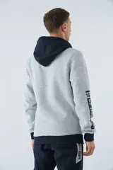 Buzo canguro gris con capucha ajustable y bolsillo delantero. Tiene puños y cintura acanalados en azul marino, y un parche con texto en el pecho.