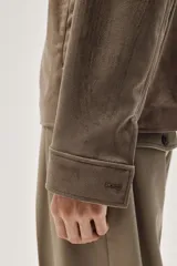 Campera marrón con cuello clásico y cierre frontal. Tiene bolsillos insertados al bies con botón a presión, bolsillo interior y botón en los puños. Corte estándar y forro interior.