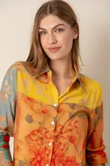 Camisa de manga larga con cuello clásico y botones frontales. Presenta un estampado floral multicolor en tonos amarillo, naranja, celeste y rojo.
