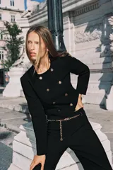 Blazer corta negra de cuello redondo y manga larga, con cierre frontal cruzado con botones dorados y falsos bolsillos delanteros.