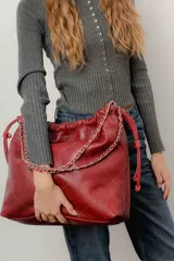 Bolso tipo tote de cuero color rojo con diseño acolchado y cadena plateada en las asas.