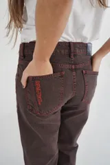 Pantalón de jean marrón de corte recto y tiro medio, con costuras en color naranja y texto estampado en el bolsillo trasero.