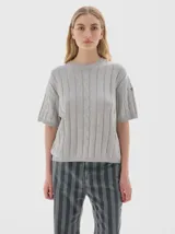 Remera de punto negra con cuello redondo y mangas cortas. Presenta un diseño de tejido con trenzas verticales.