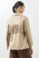 Chaqueta color beige de simil gamuza con flecos en mangas y ruedo, con cuello camisero y cierre frontal con botones.