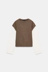 Prenda de manga larga blanca con un chaleco de tejido de punto azul marino superpuesto, creando un efecto de dos piezas. El chaleco es de cuello redondo y corte recto.