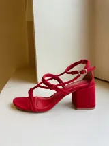 Sandalias rojas de cuero, con tiras finas con nudos en el empeine y pulsera con hebilla en el tobillo. Taco cuadrado de 7 cm.