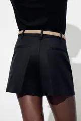 Bermuda color crema de tiro medio con pinzas delanteras y cinturón fino color beige. Tiene bolsillos frontales y falsos bolsillos de vivo en la espalda.