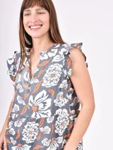 Vestido negro corto con volados en las mangas y escote en V con botones. El cuerpo es suelto con un corte a la altura de la cadera que genera un volante fruncido en la falda.