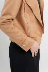 Chaqueta color beige de tela tipo gamuza con elastano, cuello solapa, manga larga con trabillas en hombro, bolsillos delanteros con cremallera metálica y cierre frontal con cremallera.