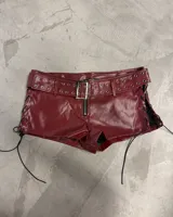 Shorts de efecto cuero color bordó con talle alto. Presenta un cinturón incorporado con hebilla metálica y ojales a lo largo del borde del cinturón y la cintura. Los laterales tienen cordones negros para ajustar el calce.