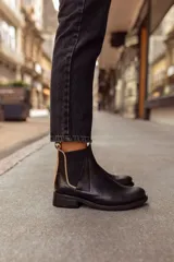 Botas Chelsea negras de cuero con elástico lateral y tirador trasero en color tostado. El talón tiene un detalle de cuero texturizado.