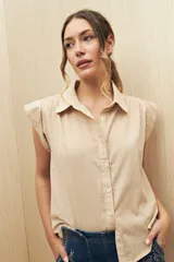 Camisa color beige, de corte recto, con cuello clásico, mangas cortas con volados en los hombros y cierre frontal con botones.