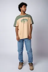 Remera color beige con mangas y parte superior en verde militar. Estampado frontal con texto "Lucky" y diseño de flores con rostro.