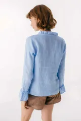 Blusa blanca de lino con botones de nácar, volados en el escote y mangas largas con puños acampanados. Corte recto y holgado.