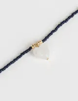 Collar corto de mostacillas azul marino con dije de corazón blanco y detalles dorados.