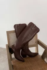 Bota de cuero marrón con caña alta, punta fina y taco bajo.