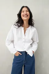 Camisa blanca de algodón con cuello mao con leve frunce, abotonadura frontal con botones de nácar y mangas amplias con puños fruncidos.