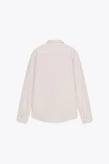 Camisa color crudo de corte recto, con cuello clásico, manga larga con puños abotonados, cierre frontal con botones y bolsillo de parche en el pecho.