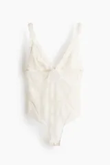 Body blanco de encaje con breteles finos ajustables y escote en V. Copas sin aros, forradas en malla, que confieren al busto una forma natural y una sujeción liviana. Cierre de corchete en la espalda. Refuerzo interior con botones a presión ocultos y corte alto atrás.