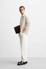 Camisa de hombre regular fit, color blanco con rayas verticales negras, cuello solapa, manga larga con puños abotonados y cierre frontal con botones.