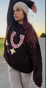 Sweater marrón tejido a mano con diseño de herradura fucsia y estrellas crudas.