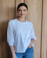 Remera blanca de algodón con mangas 3/4 abullonadas y cuello redondo. Presenta costuras a contratono en ruedo y cuello.