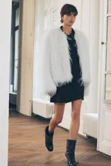 Chaqueta de pelo sintético color blanco, de cuello redondo y manga larga. Tiene bolsillos delanteros, forro interior y cierre frontal con ganchos metálicos forrados.