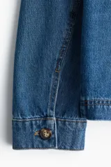 Campera azul de denim con cuello clásico, cierre frontal con botones dorados, dos bolsillos de parche en el pecho y dos bolsillos ribeteados en la cintura.