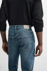 Pantalón de jean azul oscuro, corte slim fit, tiro medio, cinco bolsillos, tejido elástico y efecto lavado.