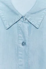 Mono corto de tela celeste, con cuello solapa, mangas cortas con dobladillo y cierre frontal con botones. Tiene un bolsillo de parche en el pecho.