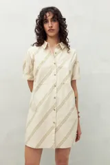 Vestido camisero corto color verde claro con estampado de hojas en blanco. Tiene cuello camisero, cierre frontal con botones y corte recto.