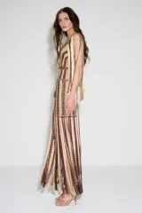 Vestido largo tejido a mano con diseño a rayas verticales en tonos beige y marrón oscuro. Presenta escote en V, ajuste entallado en el torso y falda con flecos largos que caen desde la cadera.