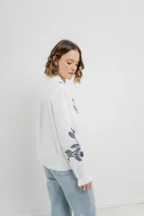 Camisa de manga larga en algodón liviano, color azul marino, con bordados florales en contraste en el frente y mangas. Cuello mao con terminación en ondas y puños fruncidos.