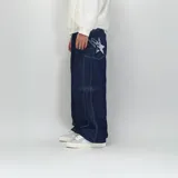 Pantalón de jean azul oscuro, corte ultra baggy, con costuras blancas a contraste y un rayo bordado en el bolsillo lateral.