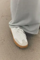 Zapatillas deportivas blancas con suela marrón en contraste y detalle de estampado animal en la parte trasera.