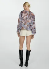 Blusa de gasa estampada con motivos paisley en tonos marrón, celeste y rosa. Tiene escote en V con volantes, mangas largas con puños elásticos y corte holgado.