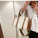 Bolso tipo tote color beige con laterales negros, doble asa corta de mano con detalles en cuero sintético negro y correa larga de hombro negra regulable y extraíble.