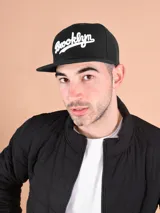Gorro negro con visera plana y bordado frontal con la palabra "Brooklyn" en blanco.