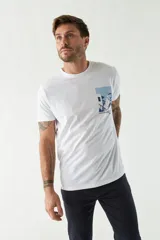 Remera blanca de algodón con estampado de una casa de playa en tonos azules. Corte regular, manga corta y cuello redondo.