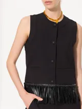 Chaleco corto color crudo, confeccionado en twill, con ruedo terminado en flecos de cuerina al tono y acceso delantero mediante botones forrados con tela base.